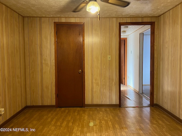 empty room featuring wooden walls, light hardwood / wood-style flooring, a textured ceiling, and ceiling fan