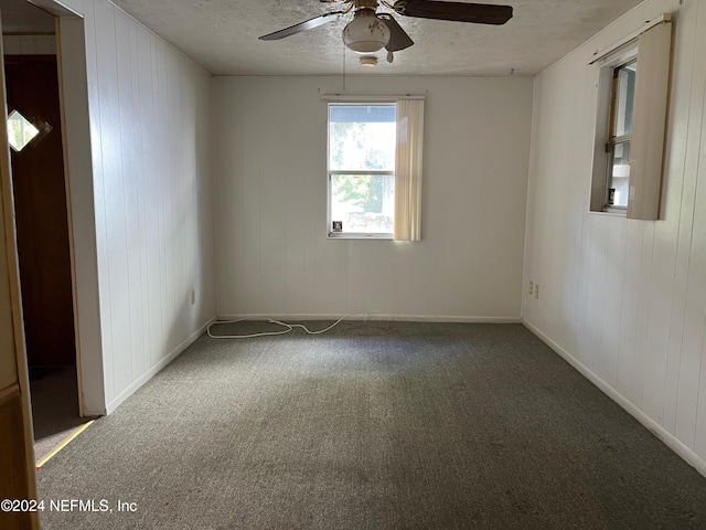 unfurnished room with carpet, a textured ceiling, wooden walls, and ceiling fan