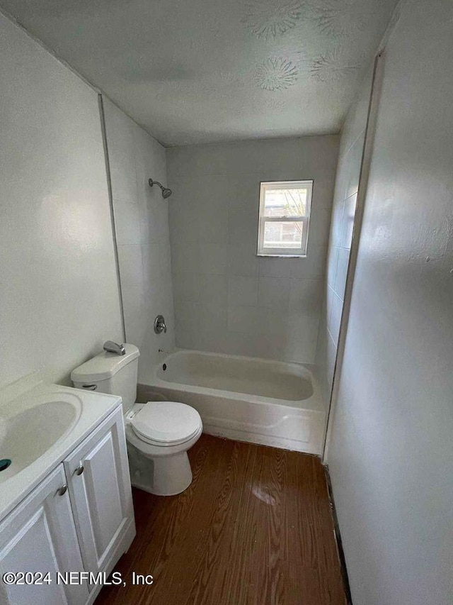 full bathroom featuring hardwood / wood-style floors, a textured ceiling, toilet, vanity, and tiled shower / bath combo