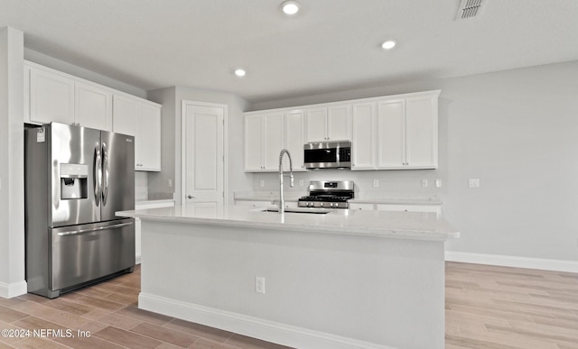 kitchen with white cabinetry, an island with sink, stainless steel appliances, and light wood-type flooring