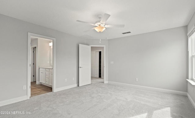 unfurnished bedroom with ceiling fan, ensuite bathroom, and light carpet