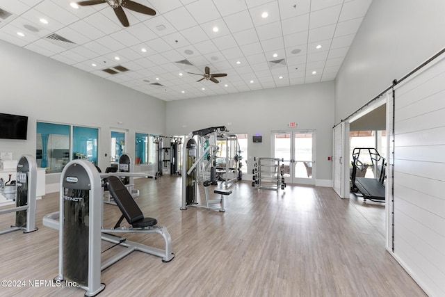 exercise room featuring ceiling fan, a towering ceiling, and light hardwood / wood-style floors