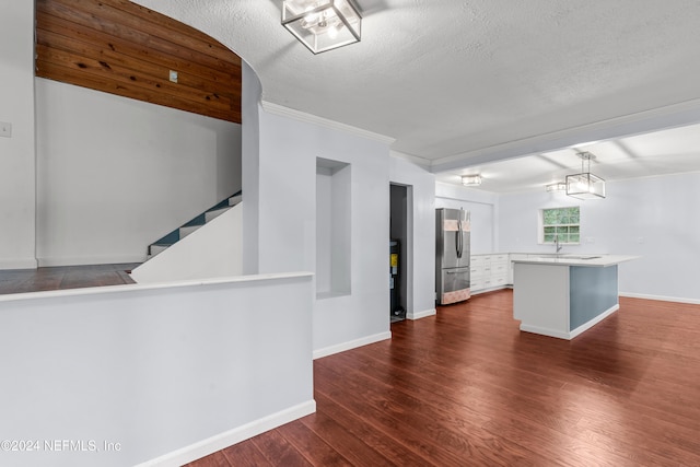 kitchen with a center island, ornamental molding, decorative light fixtures, dark wood-type flooring, and stainless steel refrigerator