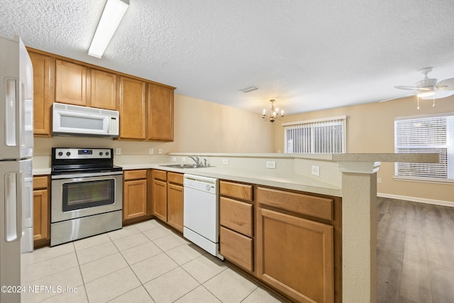 kitchen featuring kitchen peninsula, a textured ceiling, white appliances, sink, and light hardwood / wood-style flooring