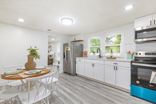 kitchen with sink, appliances with stainless steel finishes, light hardwood / wood-style flooring, and white cabinetry