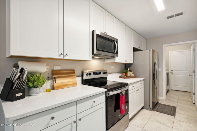 kitchen with light stone countertops, white cabinetry, stainless steel appliances, and light tile patterned flooring