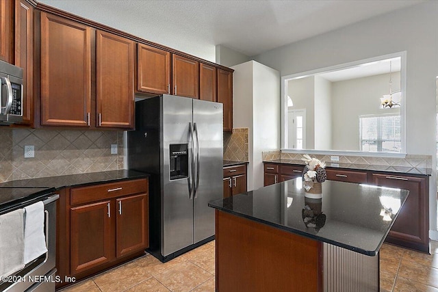 kitchen with appliances with stainless steel finishes, a kitchen island, backsplash, dark stone countertops, and a chandelier