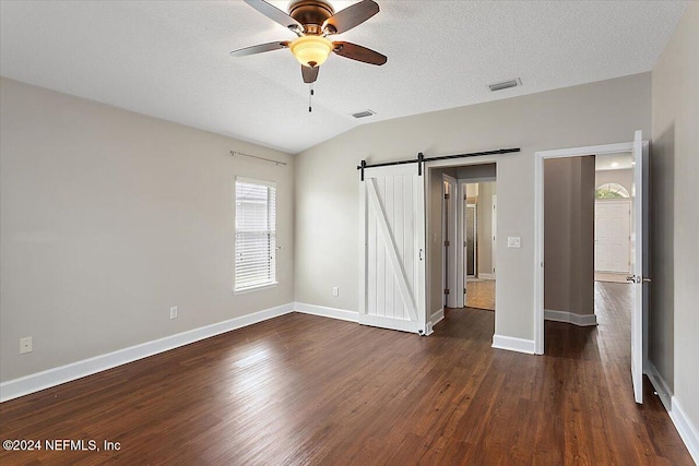 unfurnished bedroom featuring lofted ceiling, ceiling fan, a textured ceiling, a barn door, and dark hardwood / wood-style floors