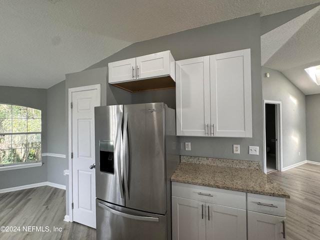 kitchen featuring light stone countertops, light wood-type flooring, lofted ceiling, white cabinets, and stainless steel fridge with ice dispenser