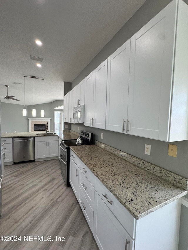 kitchen with kitchen peninsula, appliances with stainless steel finishes, white cabinetry, light wood-type flooring, and decorative light fixtures