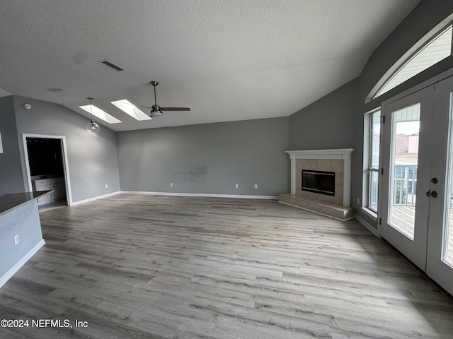 unfurnished living room featuring hardwood / wood-style floors, a tiled fireplace, ceiling fan, a textured ceiling, and lofted ceiling with skylight