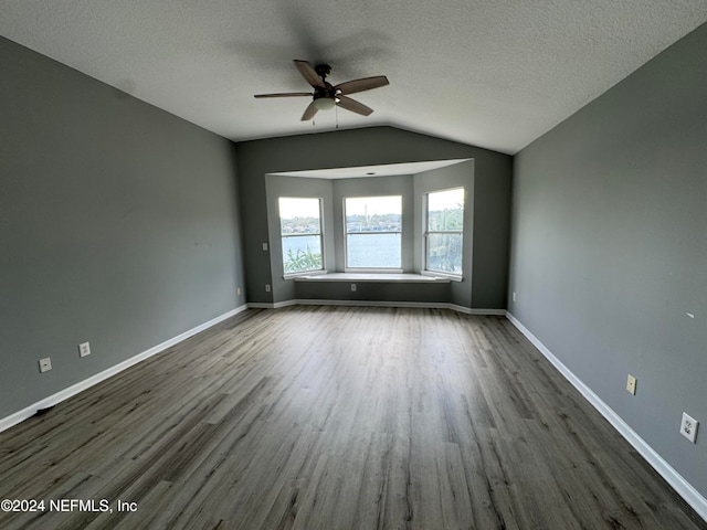 unfurnished room with dark wood-type flooring, a water view, a textured ceiling, and lofted ceiling