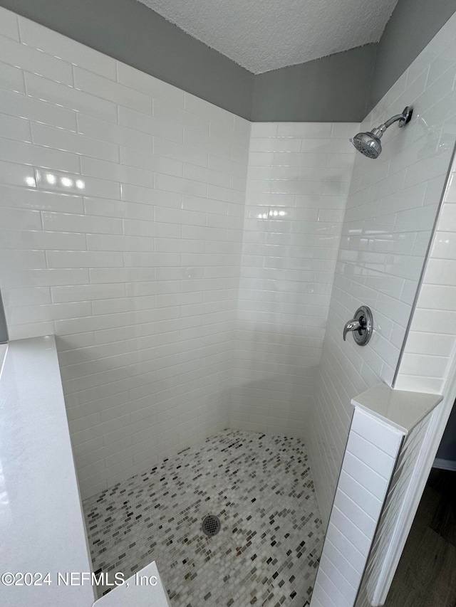 bathroom with a textured ceiling and tiled shower