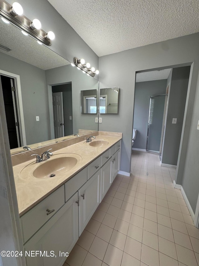 bathroom featuring a shower with door, vanity, a textured ceiling, and tile patterned floors