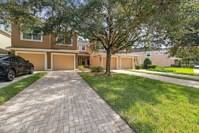 townhome / multi-family property featuring decorative driveway, a front lawn, and stucco siding