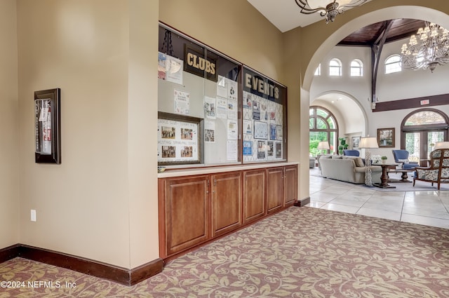 hall with light tile patterned flooring, plenty of natural light, a towering ceiling, and beam ceiling