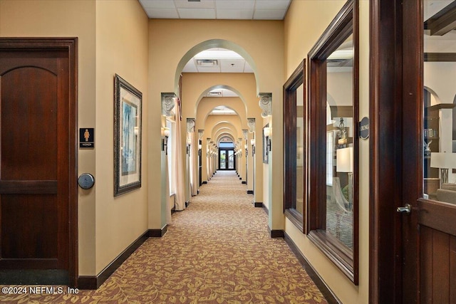 hallway with light colored carpet and a drop ceiling