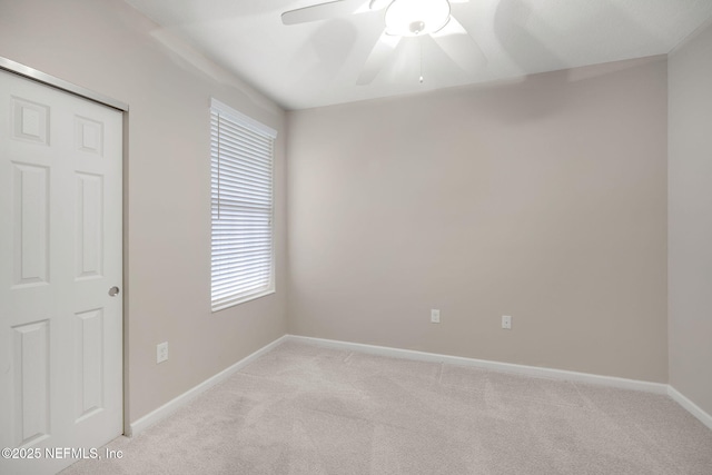 empty room featuring a ceiling fan, light colored carpet, and baseboards