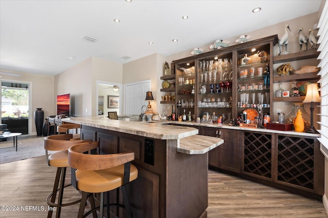 bar with dark brown cabinets, light wood-type flooring, and ceiling fan