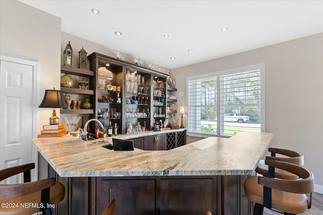 bar with light stone countertops, dark brown cabinetry, and hardwood / wood-style flooring