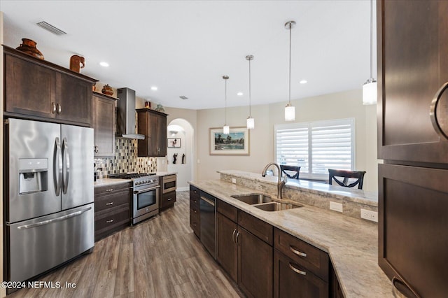 kitchen featuring wall chimney range hood, dark wood-type flooring, stainless steel appliances, sink, and decorative light fixtures