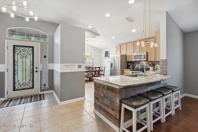 kitchen featuring stainless steel appliances, kitchen peninsula, light brown cabinets, light stone countertops, and decorative light fixtures