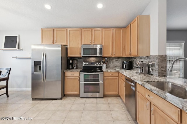 kitchen featuring stainless steel appliances, sink, light stone countertops, light brown cabinetry, and backsplash