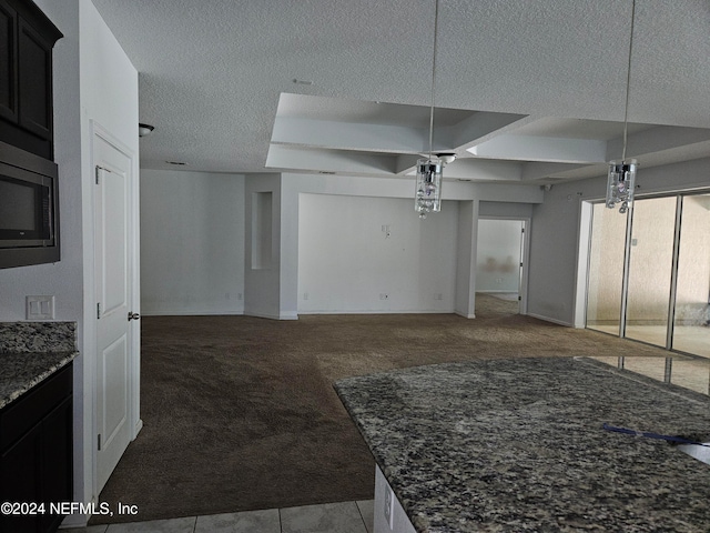 interior space with light carpet, stainless steel microwave, a textured ceiling, dark stone countertops, and decorative light fixtures