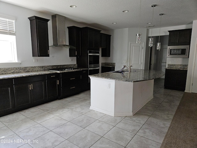 kitchen featuring appliances with stainless steel finishes, a center island with sink, wall chimney range hood, and pendant lighting