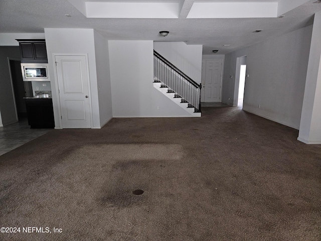 unfurnished living room with dark carpet and a textured ceiling