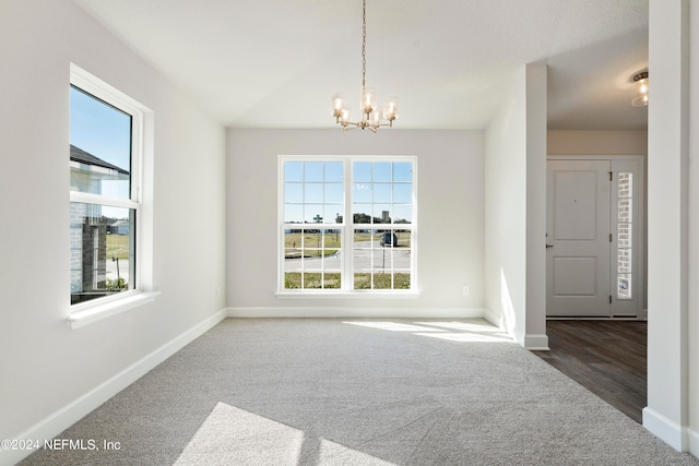 spare room featuring an inviting chandelier, baseboards, and dark colored carpet