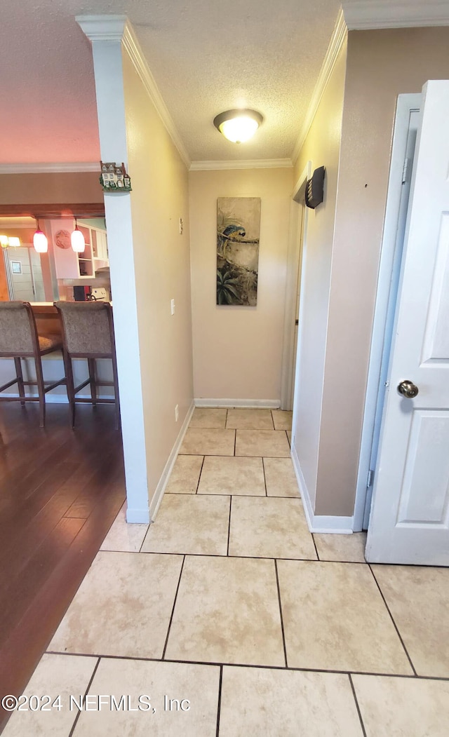 hall with a textured ceiling, ornamental molding, and light hardwood / wood-style flooring