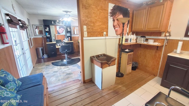 kitchen with light hardwood / wood-style flooring, a textured ceiling, wooden walls, and ceiling fan