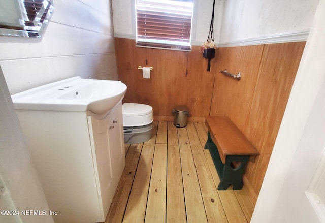 bathroom featuring vanity, toilet, wooden walls, and hardwood / wood-style floors