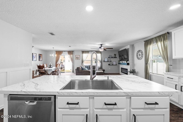 kitchen with a fireplace, white cabinetry, dishwasher, sink, and a kitchen island with sink