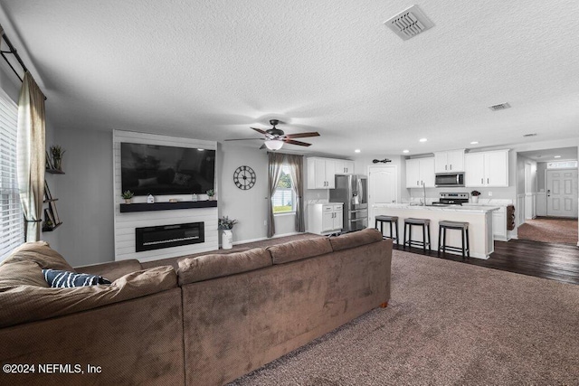 living room featuring sink, ceiling fan, a fireplace, a textured ceiling, and dark hardwood / wood-style flooring