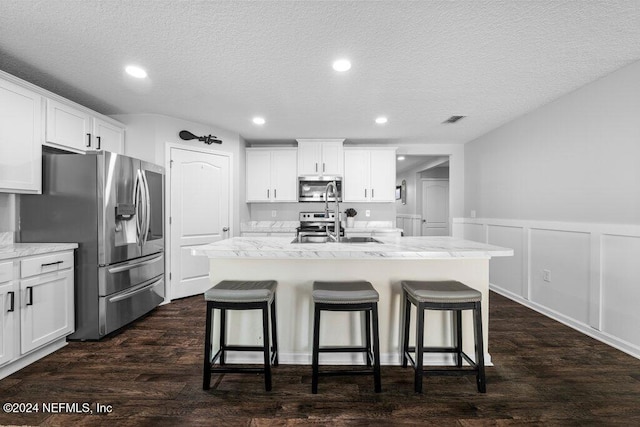 kitchen with appliances with stainless steel finishes, white cabinets, a kitchen breakfast bar, dark wood-type flooring, and a center island with sink