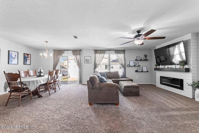 living room featuring ceiling fan with notable chandelier, a large fireplace, carpet floors, and a textured ceiling