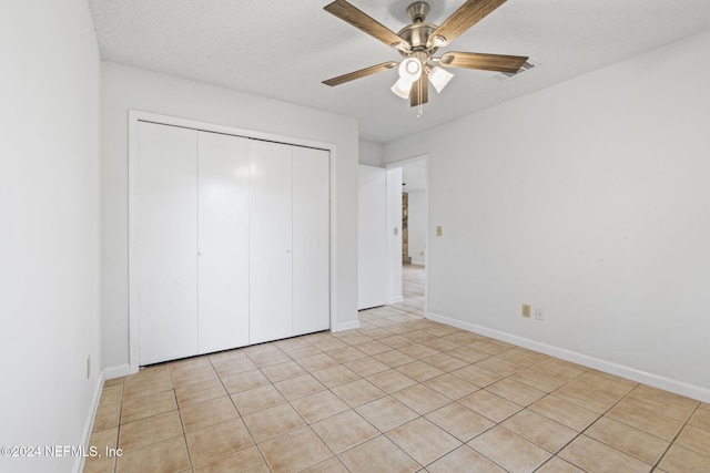 unfurnished bedroom with light tile patterned floors, ceiling fan, a textured ceiling, and a closet