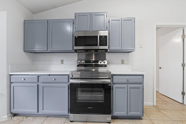 kitchen featuring stainless steel appliances, light tile patterned flooring, a textured ceiling, lofted ceiling, and gray cabinetry