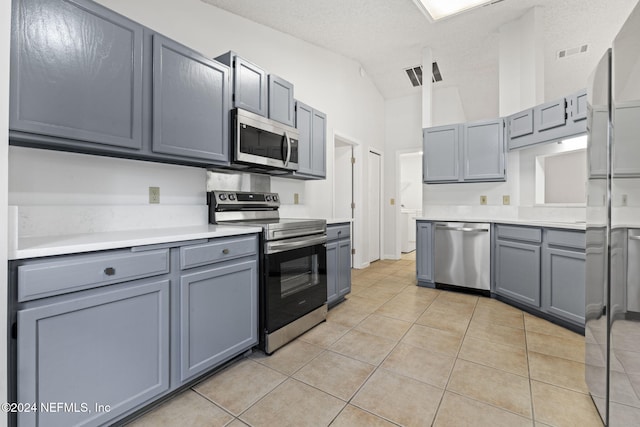 kitchen with stainless steel appliances, vaulted ceiling, a textured ceiling, light tile patterned floors, and gray cabinetry