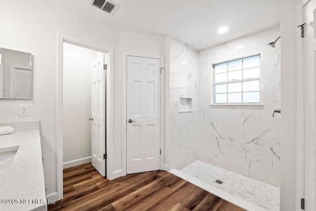 bathroom featuring vanity, wood finished floors, visible vents, a marble finish shower, and baseboards