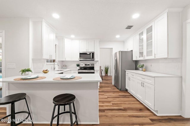 kitchen with visible vents, a peninsula, light wood-style floors, appliances with stainless steel finishes, and white cabinetry