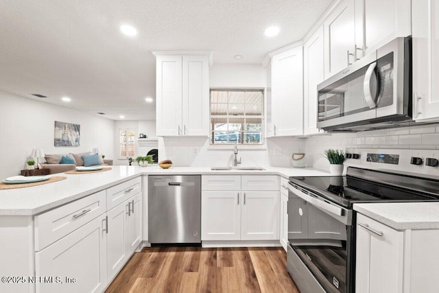 kitchen with light countertops, light wood-style flooring, appliances with stainless steel finishes, a peninsula, and a sink