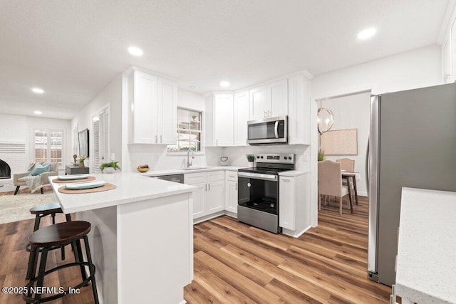 kitchen featuring a peninsula, light wood-style flooring, a sink, stainless steel appliances, and white cabinetry