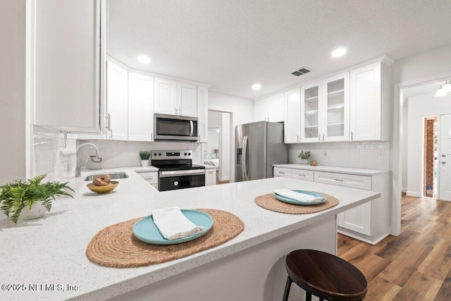 kitchen featuring a sink, wood finished floors, stainless steel appliances, white cabinets, and glass insert cabinets