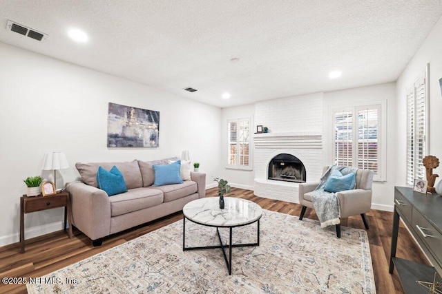 living area with visible vents, a textured ceiling, a brick fireplace, and wood finished floors