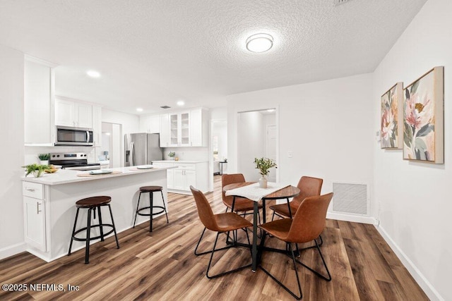 dining area featuring visible vents, a textured ceiling, wood finished floors, recessed lighting, and baseboards