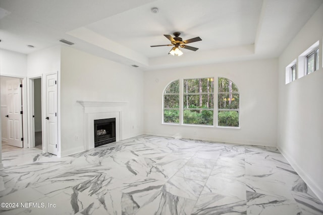 unfurnished living room with a wealth of natural light, a tray ceiling, and ceiling fan