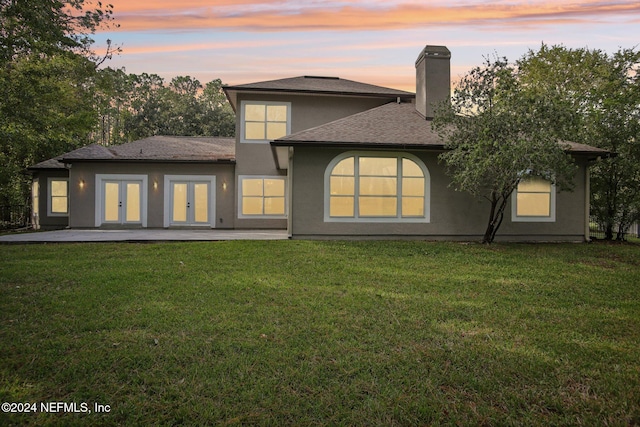 back house at dusk featuring a patio area, french doors, and a yard